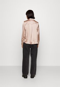 Blouse en satin à manches longues de couleur rose clair, dotée d'un pli dans le dos, d'un col et de poignets à boutons, associée à un jean en denim noir taille haute.
