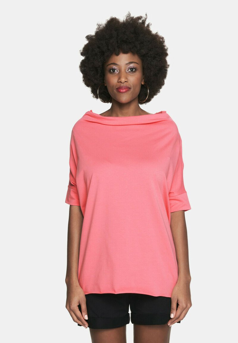 Koronkowy top z krótkim rękawem w kolorze koralowym, z szerokim, luźno opadającym dekoltem i swobodnym krojem. Miękka tkanina, w połączeniu z czarnymi szortami dla kontrastu.