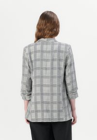 Black and white checked blazer with three-quarter sleeves, notched collar, side slits, and smooth fabric texture. Back view showcased.