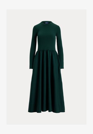 Ilgas tamsiai žalias suknelė su ilgomis rankovėmis, pagaminta iš lygios medžiagos, su prigludusiu liemeniu ir išplatėjusia, sulankstyta sijonu. Apvalus kaklas.