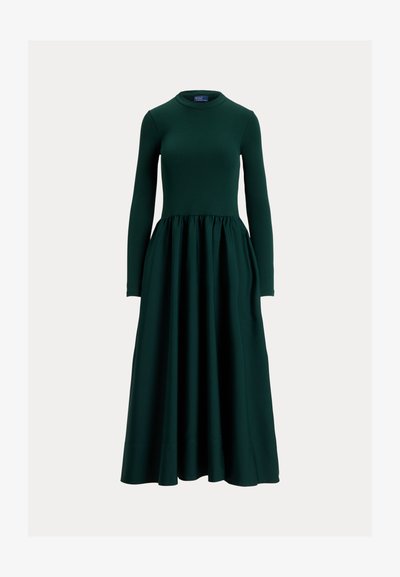 Mörkgrön dresses med lång ärm i slät tyg, med figursydd överdel och kjol som är utsvängd och rynkad. Rund halsringning.