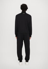 Svart sweatshirts och matchande joggers tillverkade av mjukt tyg. Har en hög krage och ribbade ärmslut. Minimalistisk design med subtil branding.