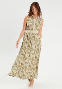 Sleeveless maxi dress in olive green with a white floral pattern, featuring a button-up front, cinched waist, and a flowing skirt.
