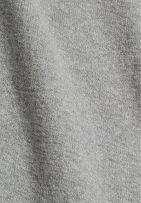 Gros plan sur un tissu tricoté doux gris clair avec une texture fine et uniforme et un motif de maille subtil visible.