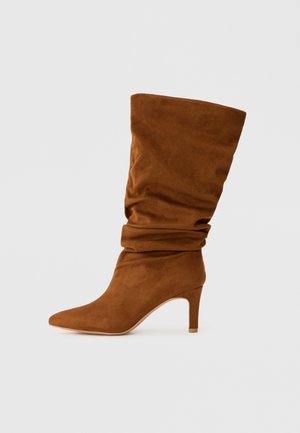 Brown suede knee-high boot with a slouchy design, pointed toe, and a slender high heel. Smooth texture with no visible patterns or accents.
