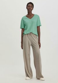 Groene V-hals T-shirt van lichte stof, gecombineerd met beige broek met touwtjes. De outfit heeft een wijde broekspijpenontwerp en een casual pasvorm.