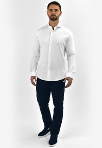 Witte button-up shirt met een gladde structuur, lange mouwen en een klassieke kraag, gecombineerd met donkere broeken en zwarte instappers.