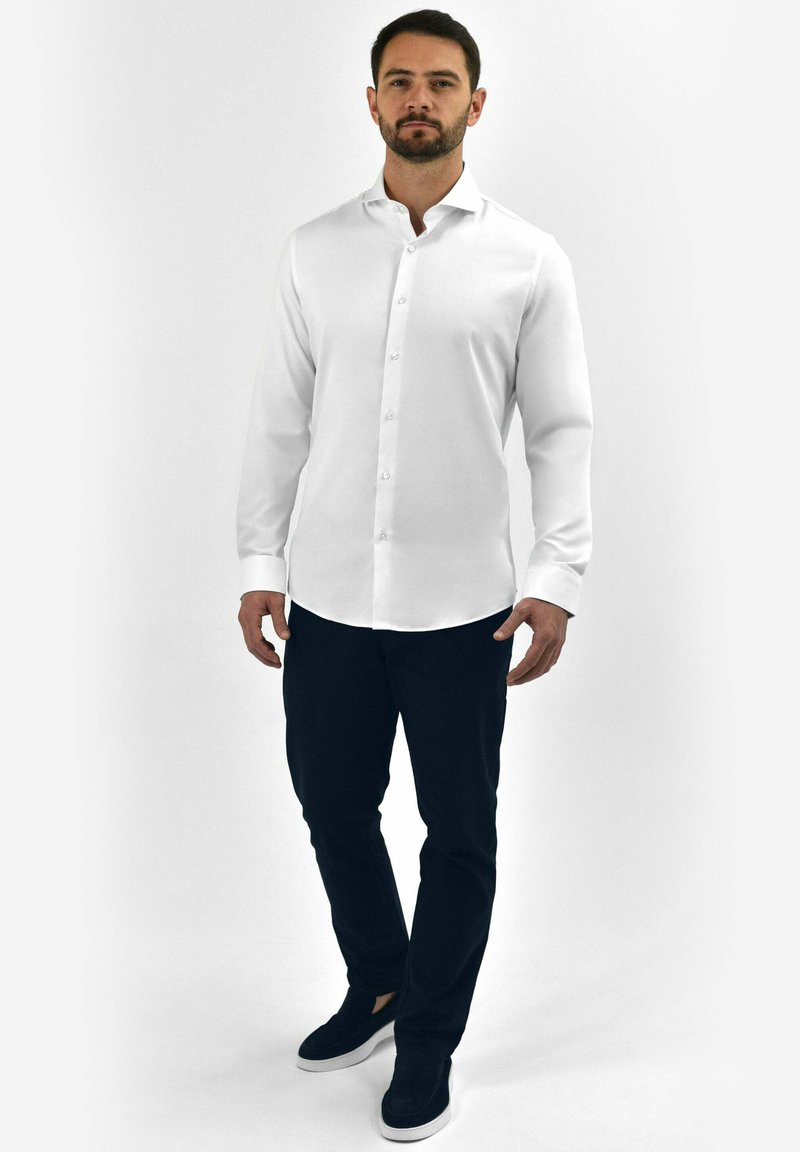 Witte button-up shirt met een gladde structuur, lange mouwen en een klassieke kraag, gecombineerd met donkere broeken en zwarte instappers.