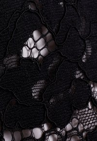 Black lace fabric featuring floral patterns with a soft, sheer texture over a lighter underlying material. Detailed stitching and open weave.