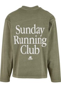 Olive zaļas krāsas krekls ar garām piedurknēm, uz kura ir balts uzraksts "Sunday Running Club" un neliels "Another Cotton Lab" logo aizmugurē.