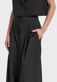 Czarna krótka marynarka z jednym guzikiem, zestawiona z wysokimi spodniami plisowanymi z bocznymi kieszeniami i gładkim wykończeniem.