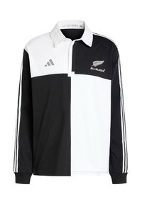 Svart och vit rugbytröja med krage, med distinkta färgblock, Adidas-logga, All Blacks-emblem och tre vita ränder på ärmarna.