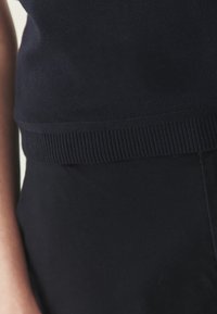 Haut en maille bleu marine foncé avec un ourlet côtelé, une texture lisse et une coupe ajustée, associé à un tissu foncé en dessous.