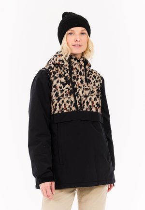 Zwarte pullover jack met een voorkant in luipaardprint, rits borstzak en verstelbare capuchon. Draagt een zwarte gebreide beanie.