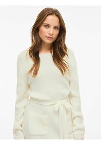 Kremasti pleteni pulover s ležernim krojem, širokim izrezom i rebrastom teksturom. Ima duge rukave i pojas u struku s prednjim džepovima.