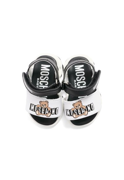Sandales pour bébé blanches et noires avec brides ajustables, ornées de graphiques d'ours en peluche et du logo "Moschino Baby" sur les brides et les semelles.