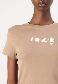 Tan fitted t-shirt made of ribbed cotton, featuring white graphic designs of a cactus, sun, wave, and shell on the front.