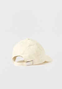 Kapa za baseball krem barve z ukrivljenim ščitnikom in nastavljivim trakom z obrobo iz kovine ter vtisnjenim logotipom na zadnji strani.