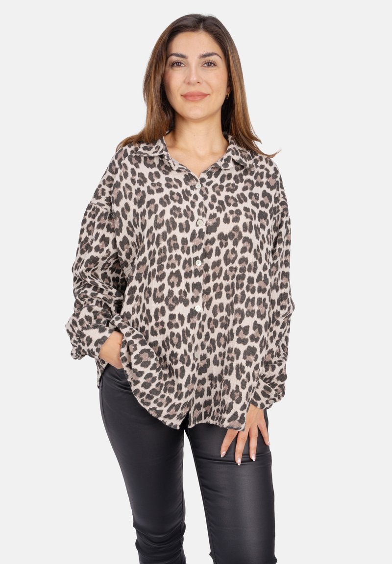 Lockere, leopardgemusterte Bluse in Beige und Schwarz mit Kragen, durchgehender Knopfleiste und hochgerollten Ärmeln, kombiniert mit schwarzen Leggings.