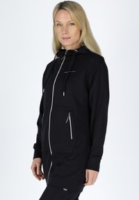 Sort zip-up hættejakke med snoretræk til hætten, to lynlåslommer foran og et logo på brystet. Glat stofstruktur.