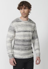 Pulover tricotat în dungi crem și gri, având un guler rotund, manșete și tiv cu margini nervurate. Fabricat din fire cu textură și modele variate.