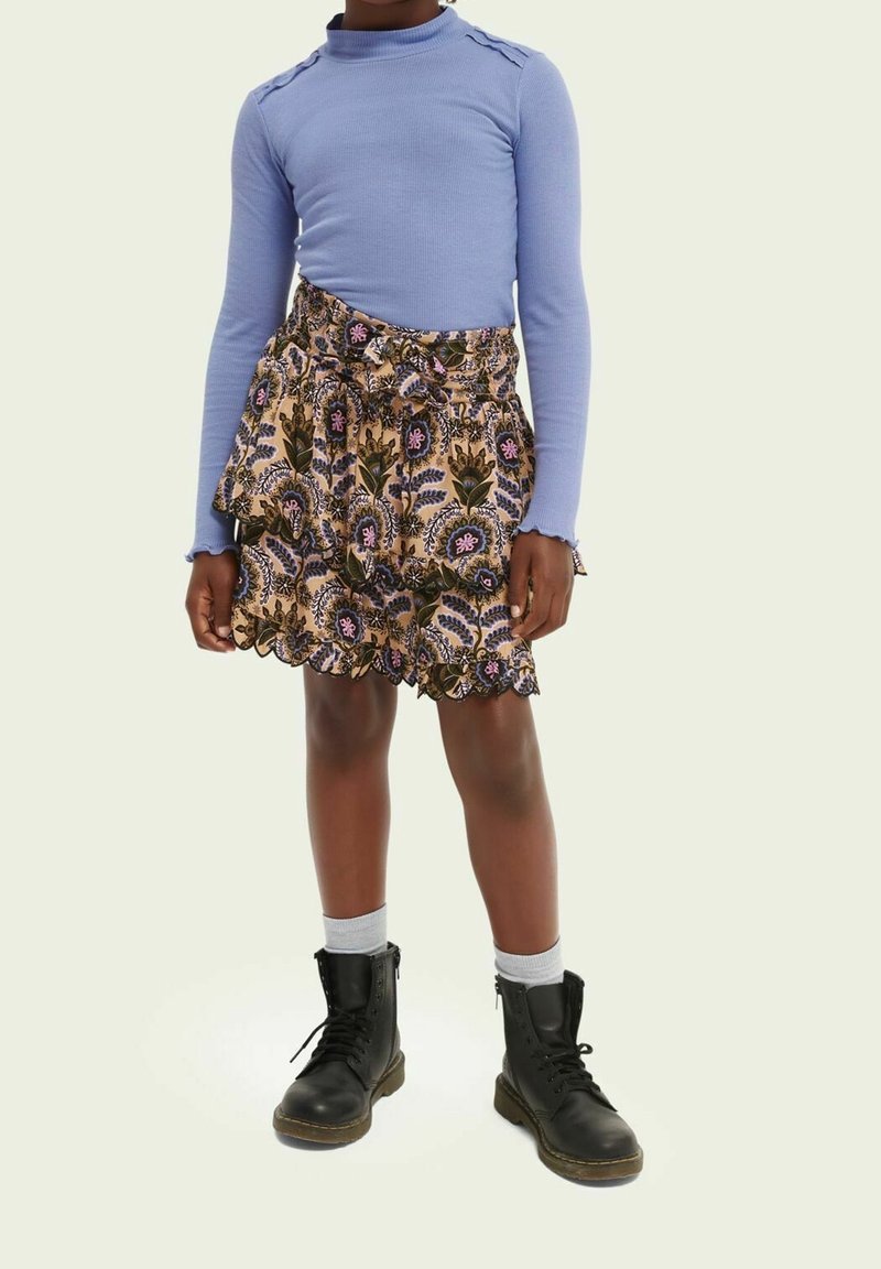 Lys blå langærmet top kombineret med et lagdelt, mønstret skørt med blomsterdesign i lilla og grøn, suppleret med sorte støvler.