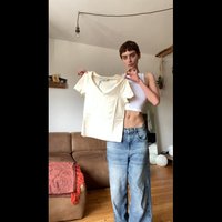 Kremfarget V-hals t-skjorte med korte ermer, glatt tekstur, vist av en person i avslappede lyseblå jeans i et rom med tregulv.