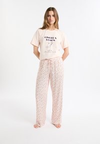 Jasnoróżowy bawełniany komplet piżamowy z krótkim rękawem i koszulką z nadrukiem oraz luźnymi spodniami z małymi kolorowymi wzorami.