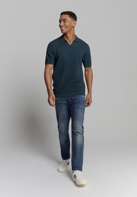 Polo shirt in donkerblauw met een gestructureerd patroon, korte mouwen en een V-hals. Gecombineerd met blauwe jeans en witte sneakers.