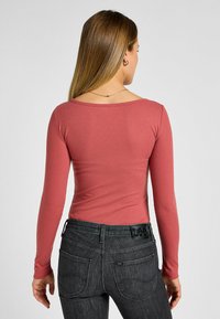 Långärmad ribbad tröja i stövrosefärg, med en rundad halsringning, tillsammans med mörkgrå jeans med synliga bakfickor och varumärkesdetaljer.