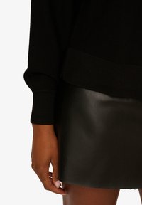 Maglione nero a maglia e gonna mini aderente in pelle nera, che mette in evidenza una consistenza liscia e un design aderente con un dettaglio sui polsini ben visibile.