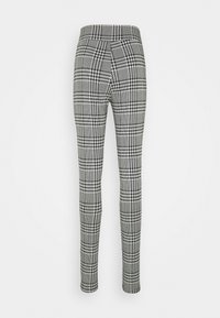 Pantaloni slim fit con motivo a scacchi e dal design houndstooth bianco e nero, con vita alta e lunghezza alla caviglia, su sfondo bianco.