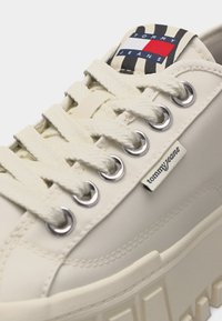 Εκρού sneaker Tommy Jeans με παχιά σόλα, κρεμ κορδόνια, ασημένια μυτερά τρύπια και ετικέτα με το λογότυπο στη γλώσσα και στο πλάι.