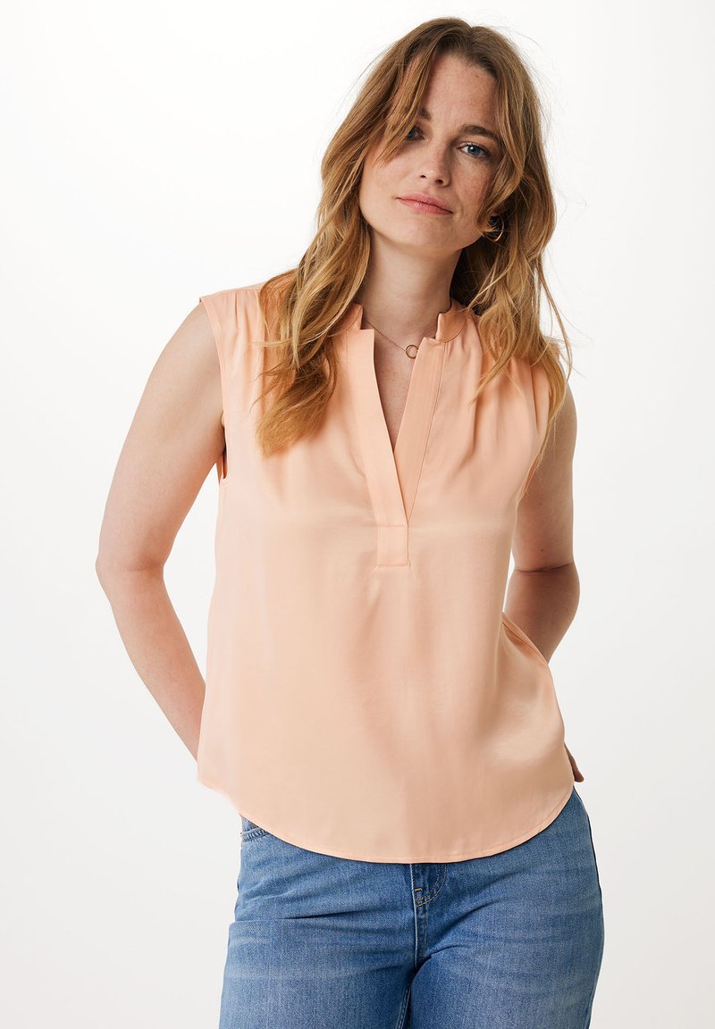 Brzoskwiniowa, bezrękawnikowa bluzka z kołnierzykiem mandarynkowym, z pionowym dekoltem oraz gładką fakturą, zestawiona z jasnoniebieskimi dżinsami.