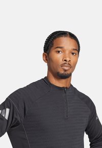 Maglia sportiva nera con zip, caratterizzata da un motivo testurizzato, maniche raglan e dettagli riflettenti sulla spalla sinistra.