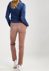 Niebieska kurtka dżinsowa o dopasowanym kroju, z guzikami w talii. Jasnoróżowe, slim-fit spodnie z tylnymi kieszeniami, z subtelnymi przeszyciami. Białe sneakersy.