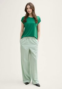 Grünes kurzärmeliges Oberteil kombiniert mit hellmintgrünen Hosen mit weitem Bein, ausgestattet mit einem elastischen Bund und seitlichen Taschen. Glatte Stoffstruktur.