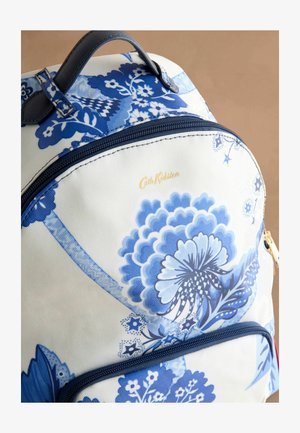 Modra nahrbtnik s cvetličnim vzorcem na belem ozadju, z glavnim predalom na zadrgo, z ročaji iz tkanine in zlatim logotipom.