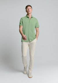 Korte mouw, lichtgroen button-up shirt met een klassieke kraag, gecombineerd met beige slim-fit broeken en lichte sneakers. Zachte stoftextuur.