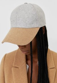 Grau-beige Kappe mit einer weichen Textur, auf der die Aufschrift "Forever Young" auf der Vorderseite gestickt ist. Mit gebogenem Schild, lässigem Design.