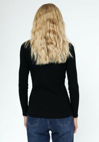 Un pull noir à côtes, à manches longues, ajusté à la taille, associé à un jean bleu. Texture douce avec un design minimal, vu de l'arrière.