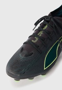 Black soccer cleat with textured synthetic upper, green accents, and laces. Features a streamlined design and cleated sole for traction.