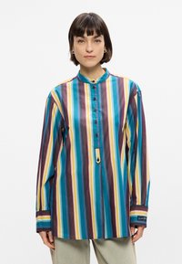 Ριγέ πουκάμισο με τερακότα, κίτρινο, μωβ και λευκές οριζόντιες λωρίδες, ψηλό γιακά, κλείσιμο με κουμπιά και μακριά μανίκια με λεπτομέρειες στις μανσέτες.