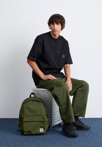 Černé oversize tričko s kapsou na prsou, olivově zelené cargo kalhoty, černé tenisky a olivově zelený batoh s logem.