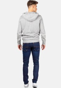 Felpa grigia con cappuccio dalla trama liscia, abbinata a jeans in denim blu scuro con tasche posteriori e dettagli di cucitura sottili.