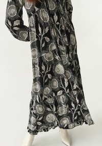 Langes schwarzes Kleid mit weißen Blumenmustern, das ein gestuftes Design und einen schmalen Saum aufweist. Der Stoff ist leicht und hat eine glatte Textur.