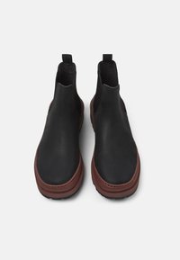 Stivali Chelsea in pelle nera con pannelli elastici laterali, suola in gomma marrone e punta arrotondata. Caratterizzati da una linguetta sul retro per un facile indossamento.