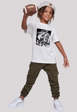 Weißes Baumwoll-T-Shirt mit einem schwarz-weißen Grafikdesign, kombiniert mit olivgrünen Cargo-Hosen und weißen Sneakers mit strukturierten Akzenten.