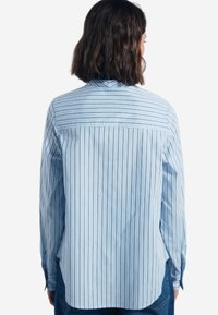 Camicia button-up azzurro chiaro con strisce verticali di un blu più scuro, caratterizzata da un design con yoke posteriore e maniche lunghe con polsini abbottonati.