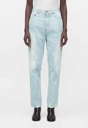 Person iført lyseblå syrevaskede jeans med høj talje, lige ben, kombineret med sorte ankelstøvler og en hvid top.